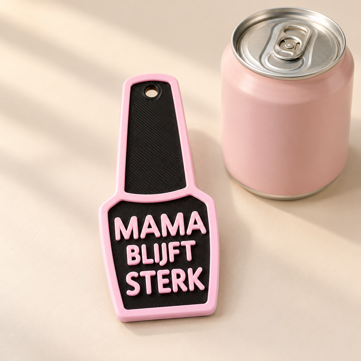 Platte MamaBlijftSterk-blikjesopener in zwart met babyroze rand en nette verhoogde letters MAMA BLIJFT STERK, naast een roze drankblikje. Het blikje is decoratie.