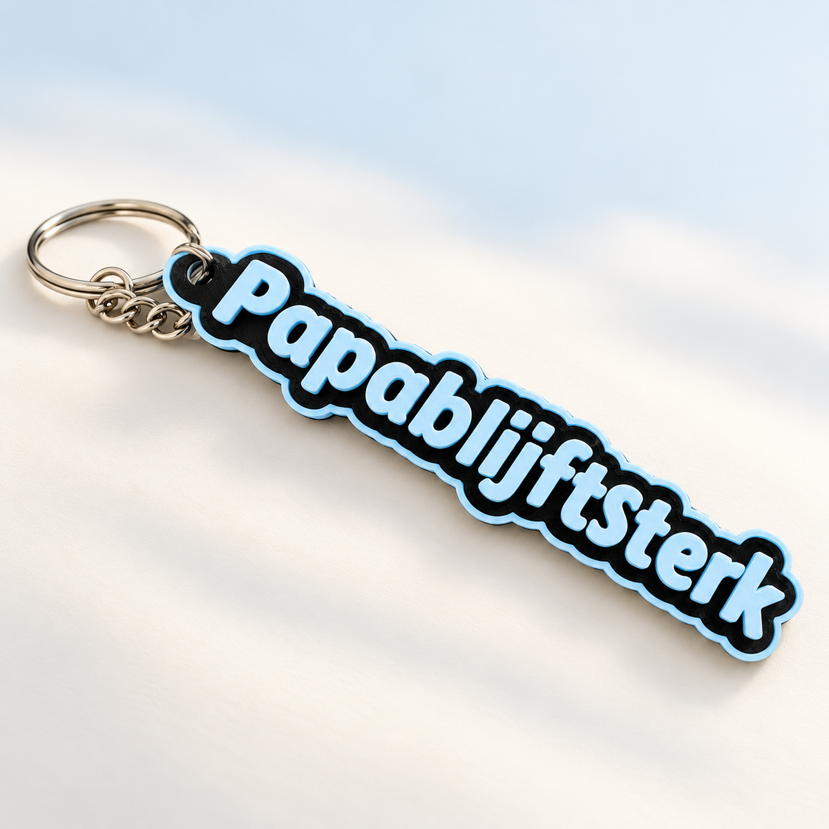 PapaBlijftSterk sleutelhanger in zwart met babyblauwe letters en rand, inclusief metalen sleutelring en kort kettinkje.